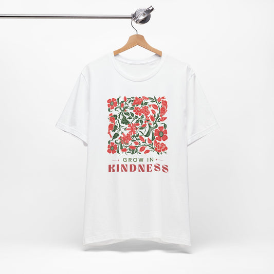 White t-shirt with floral design and 'Grow in Kindness' text on a hanger against a white background